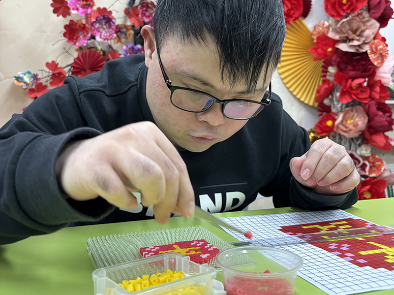 A male member wearing glasses is making bead crafts, focusing intently on his work.