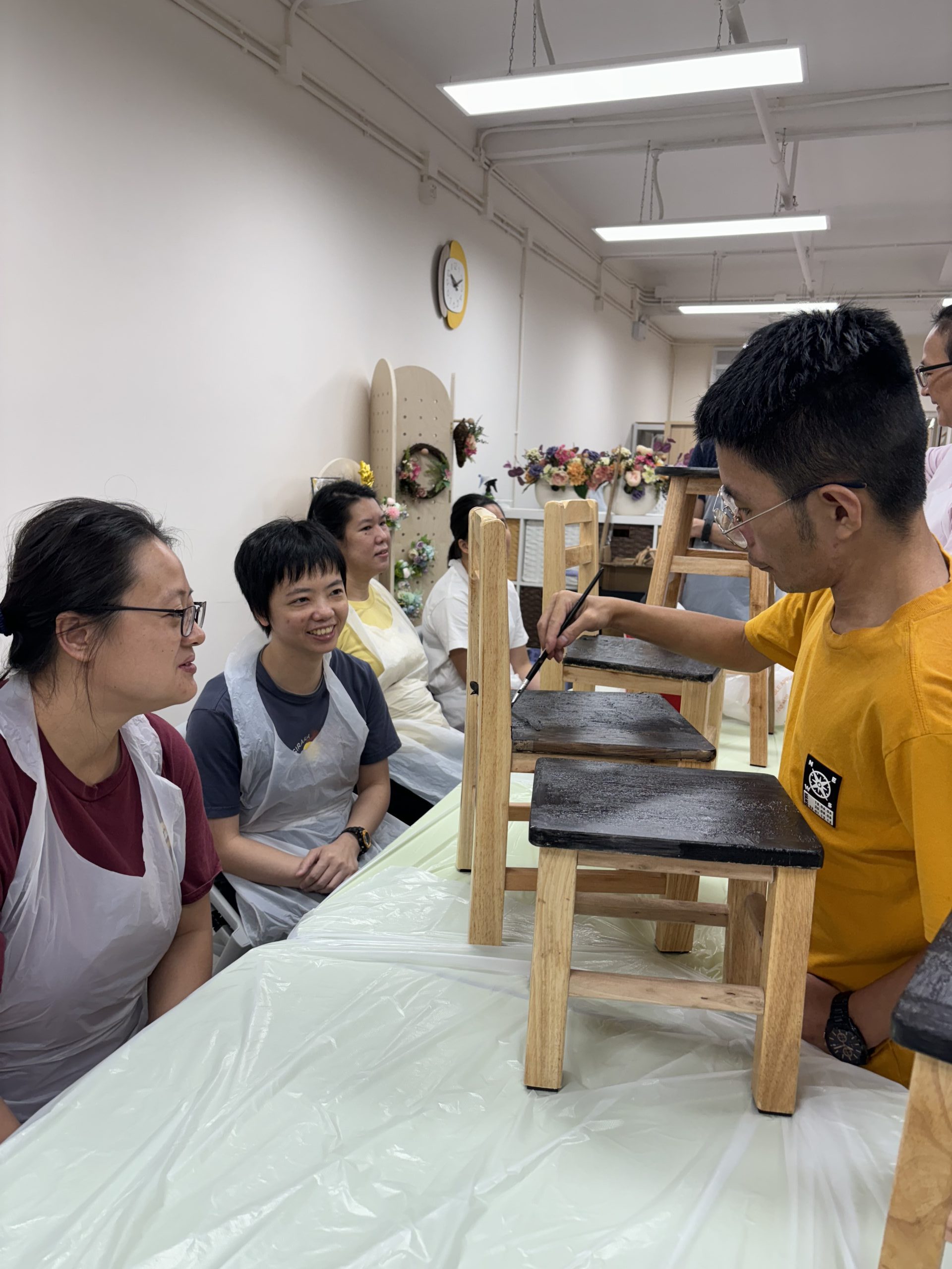 組員坐在桌子周圍，彼此交談，傾談如何塗鴉椅子，展現出和諧的社交氛圍。