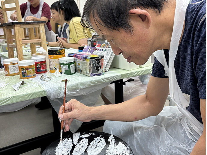 組員正專心地在用畫筆在黑色椅子上作畫，展現出他的藝術才華與創意。 