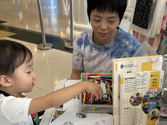 老闆Mini與一名小朋友坐在桌子旁，專注教導著兒童繪畫甜品畫。