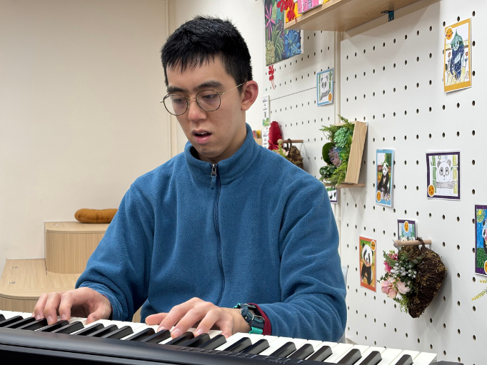 Artist Bon, wearing a blue jacket, practices playing the piano, enjoying the joy that music brings.