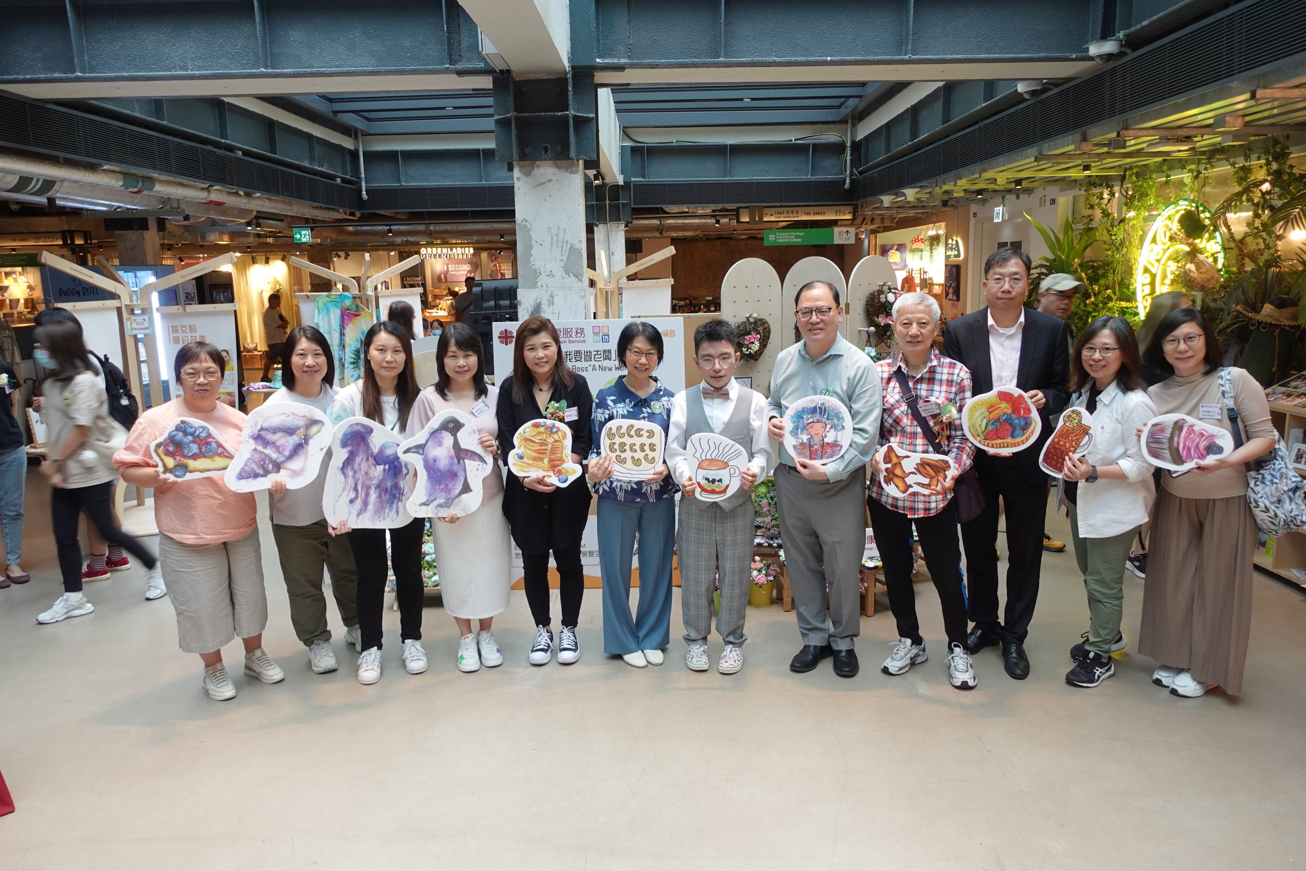 一眾會員、嘉賓、職員及義工站在我要做老闆開作業啟動禮及作品成果展的佈置前來一幅大合照。