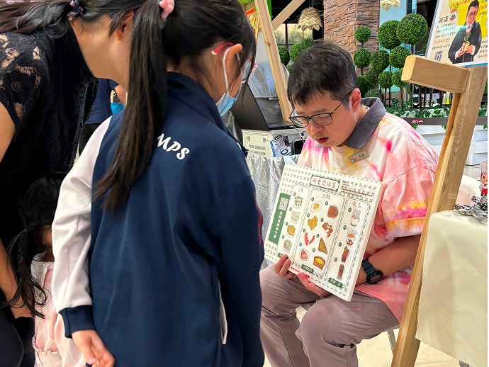 老闆阿滿手持明愛您冰室餐牌在攤位前拍照留念。