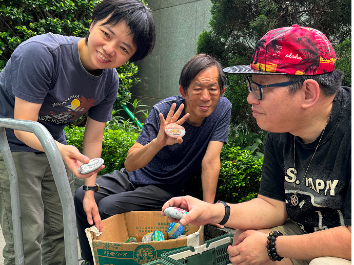 三位會員面帶笑容，合力揀選彩繪石頭，為裝飾做準備。