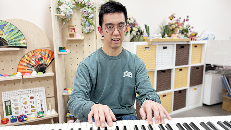 Boss Bong, wearing glasses, is intently playing the piano, demonstrating his enthusiasm and talent for music.