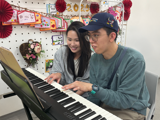 Piano teacher Ms. Lau, with a smile on her face, guides Abang in learning to play a new piece, while Abang studies diligently and is very engaged.
