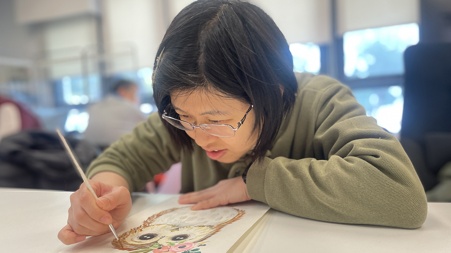 Boss KC, wearing glasses, is drawing on paper, focused on her creative process.