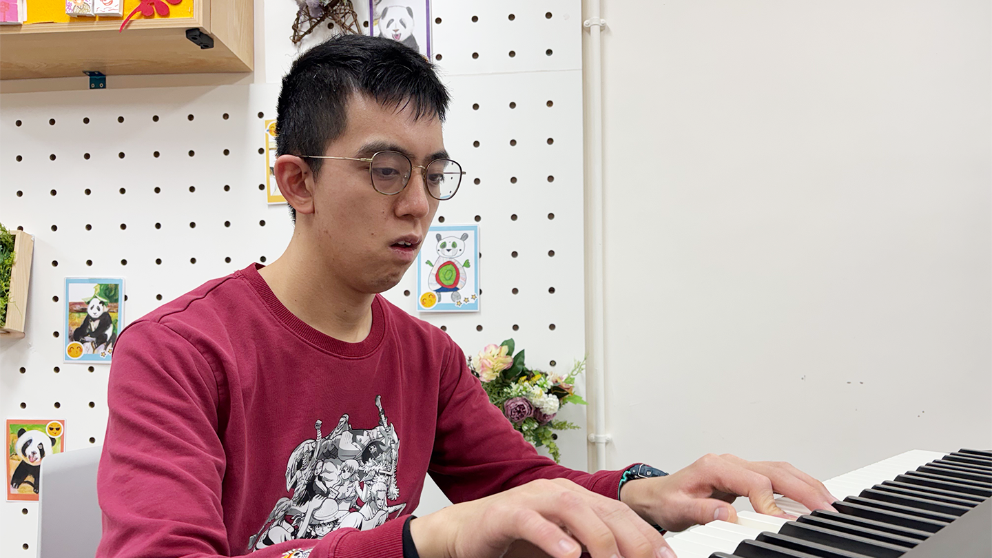 Boss Bong, wearing glasses, is focused on playing the piano, showcasing his passion and talent for music.